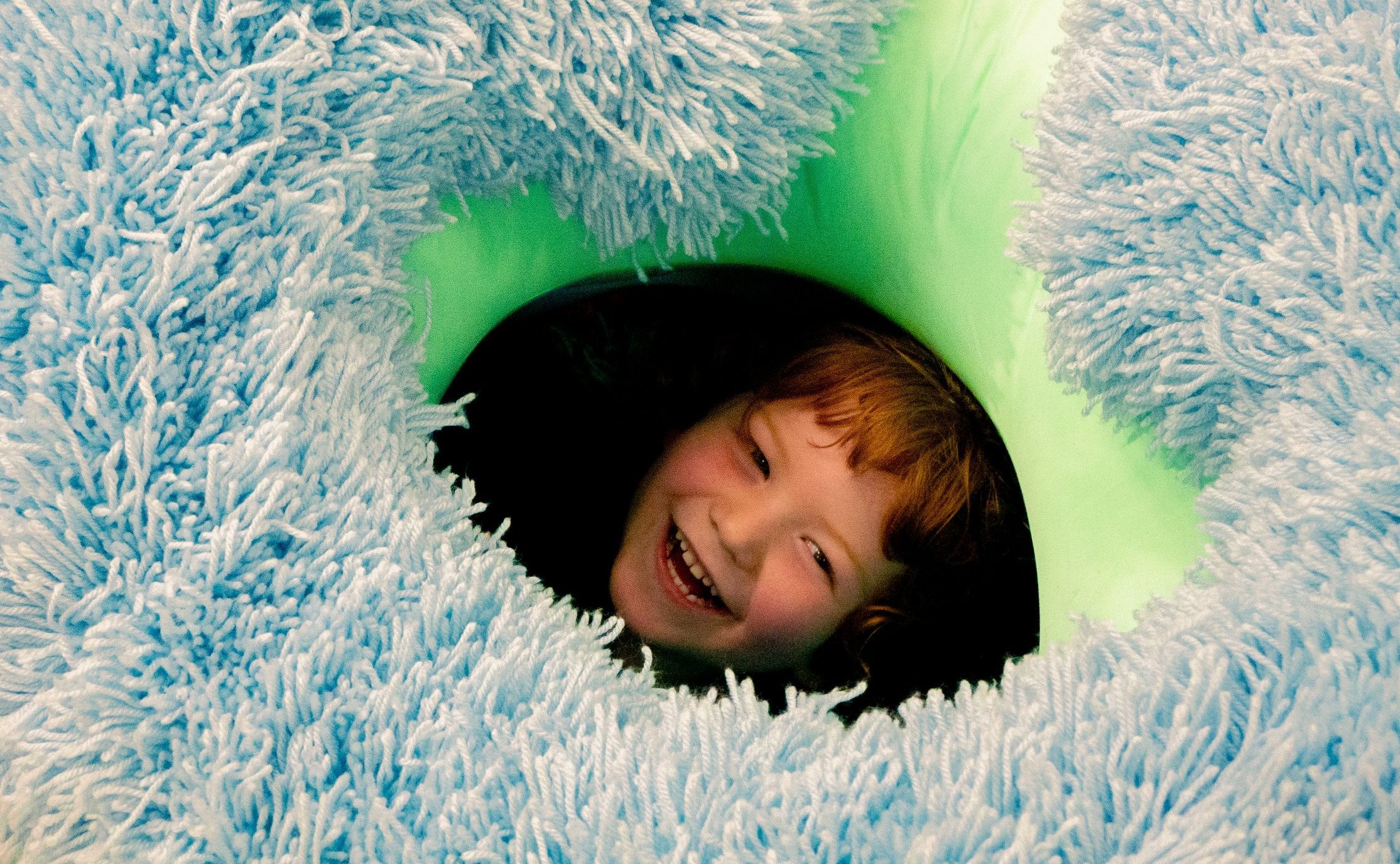 A child peaks through a pile of fluffy play cushions.