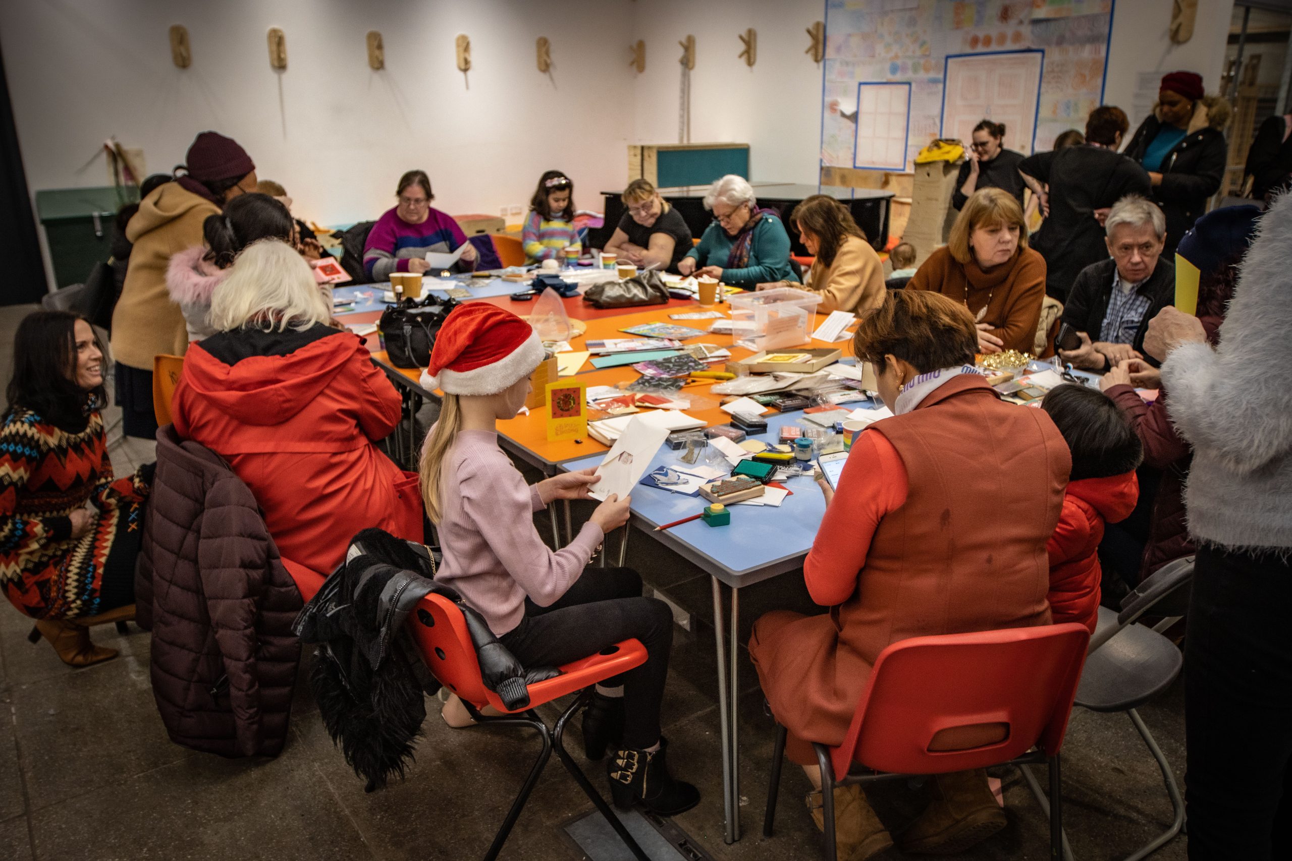 Adults and children sit together at a large table in the Useful Art Space making Christmas cards at the Multicultural Hub Christmas Lunch in 2022.