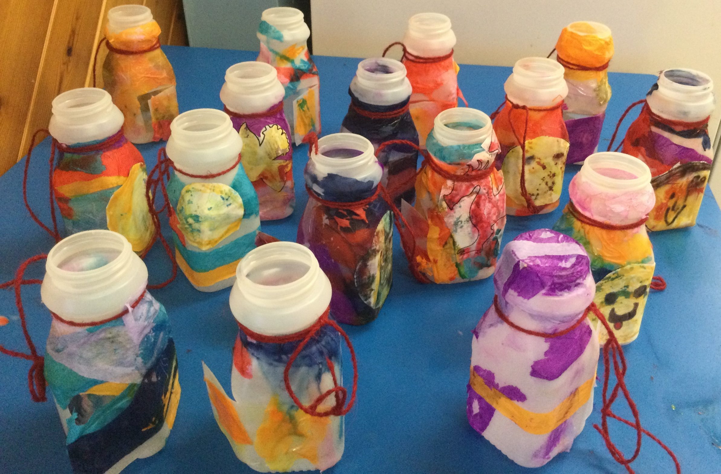 A selection of plastic bottles that have been decorated with colourful tissue paper and string to create lanterns.