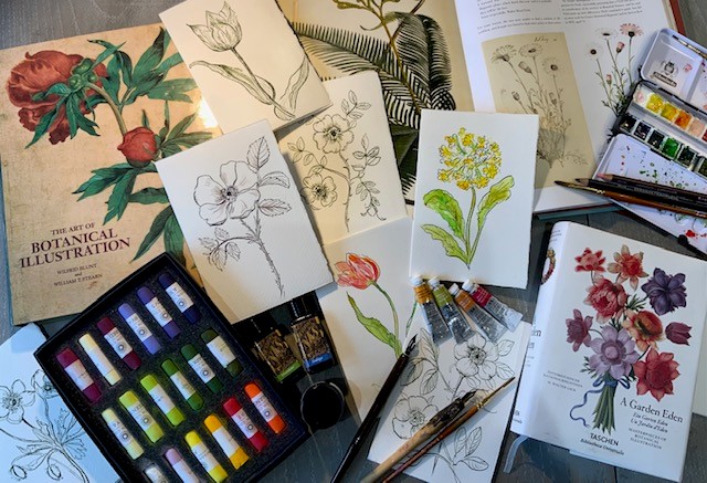 Drawings and paintings of flowers surrounded by art materials.