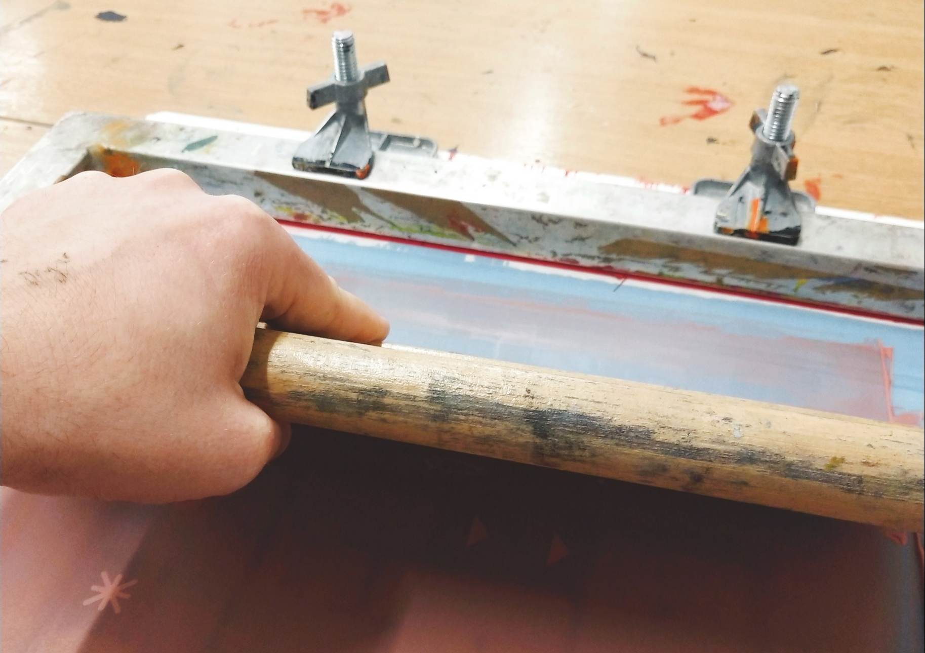 A hand holding a squeegee to create a screen print.