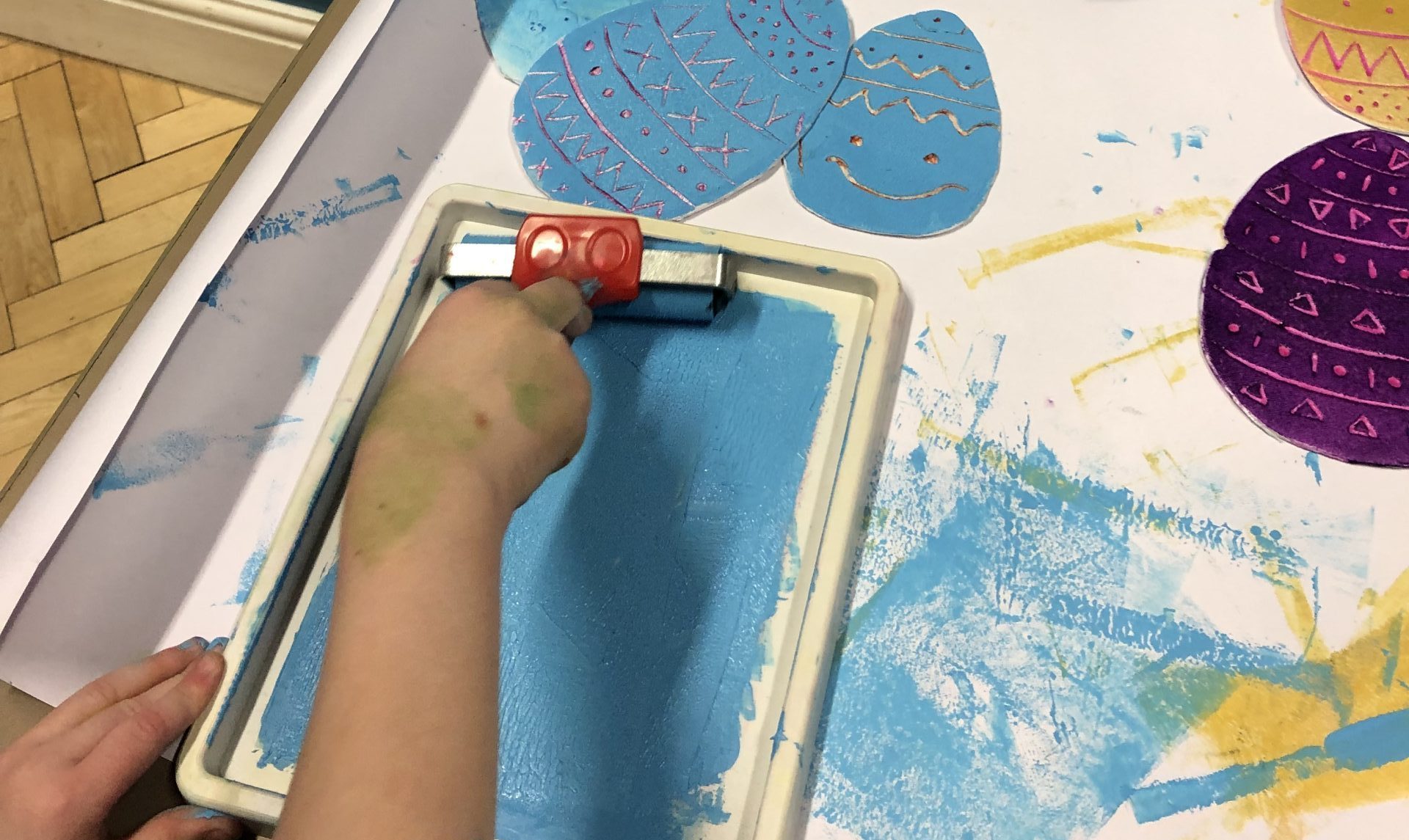 A child's hand using a roller to create a styrofoam print in blue.