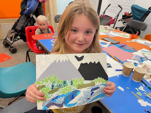 A primary school aged girl holding a collage of a mountain landscape she has made.