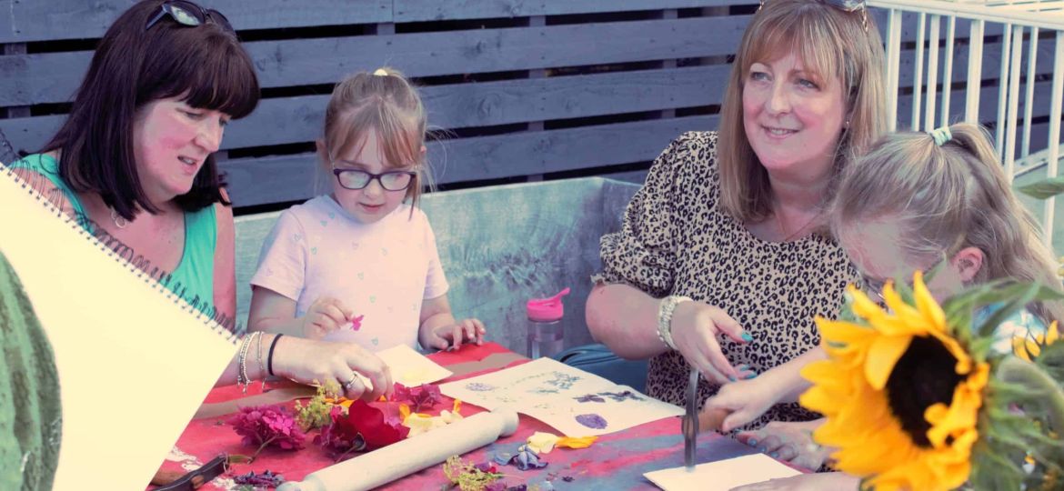 A family working on an art project in the garden. A sunflower can be seen in the bottom righthand corner.