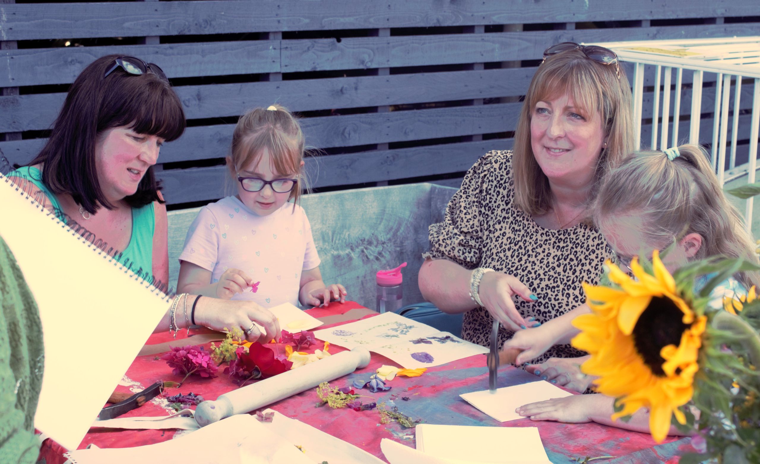A family working on an art project in the garden. A sunflower can be seen in the bottom righthand corner.