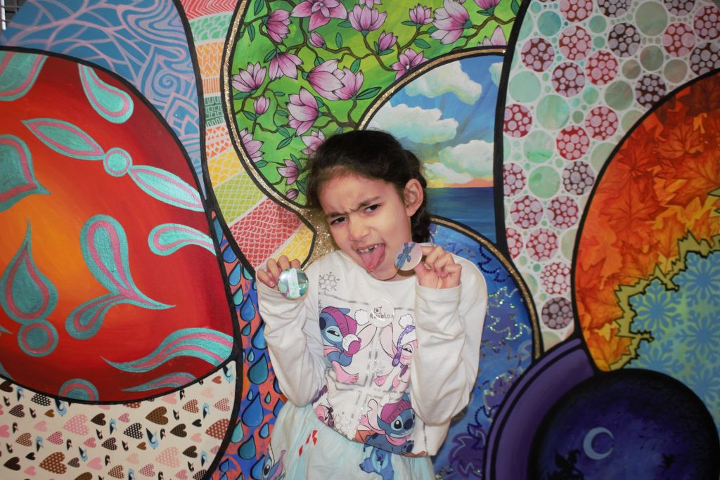A primary school aged girl pulls a funny face while holding badges she has made up to the camera.