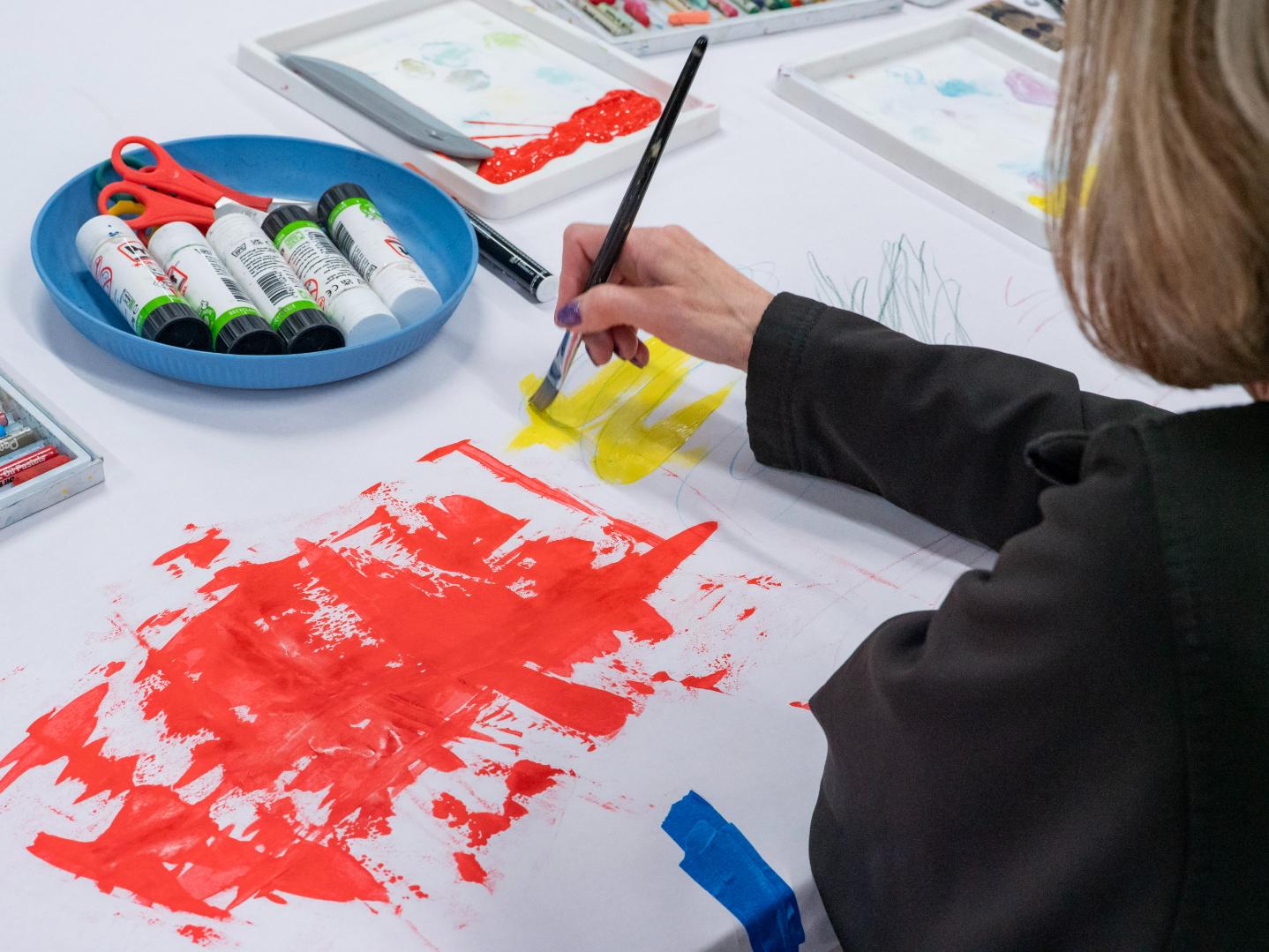 A lady works on a red and yellow abstract painting.