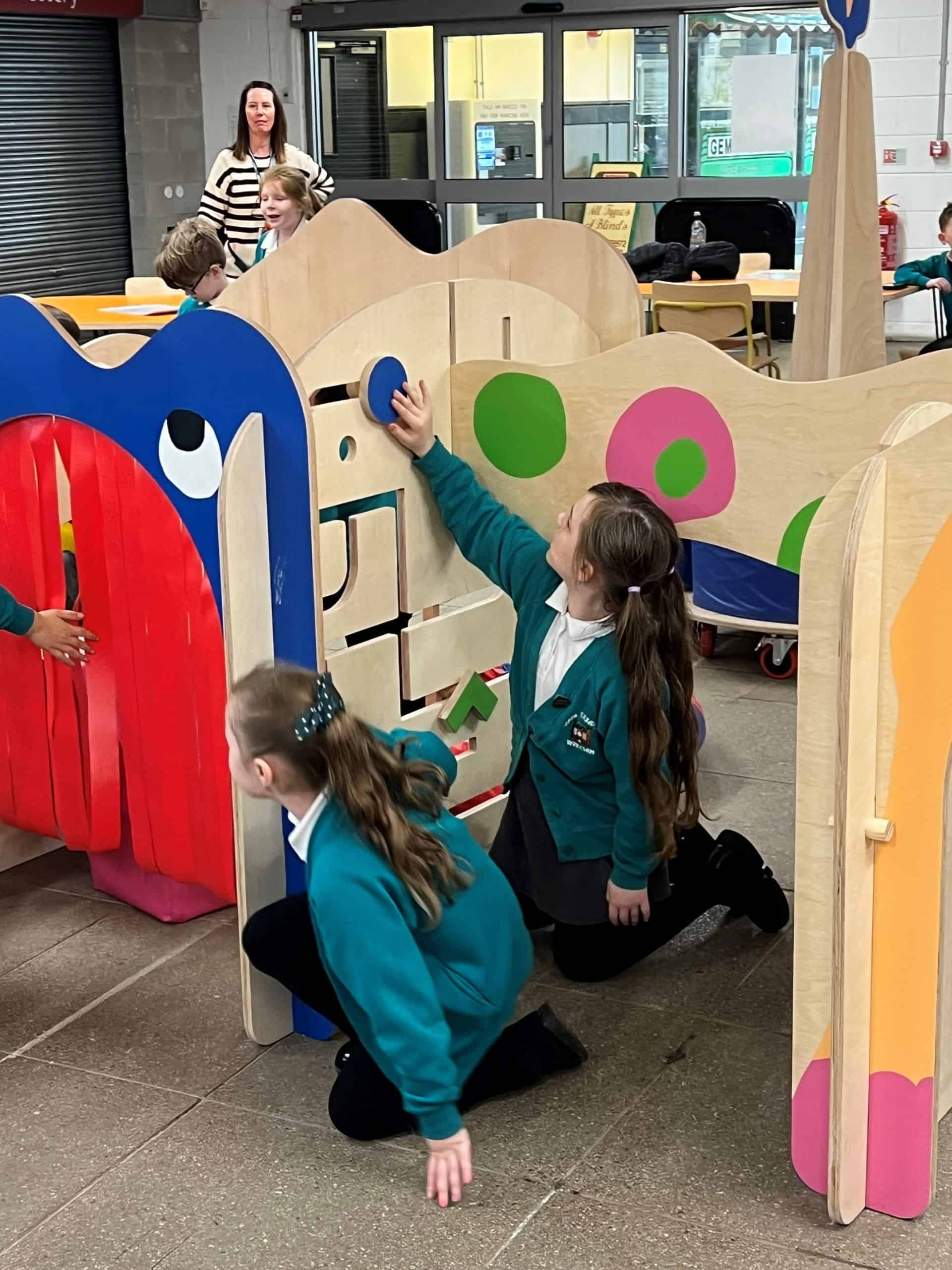 Two primary school aged girls playing with a puzzle mounted on a wooden play structure.