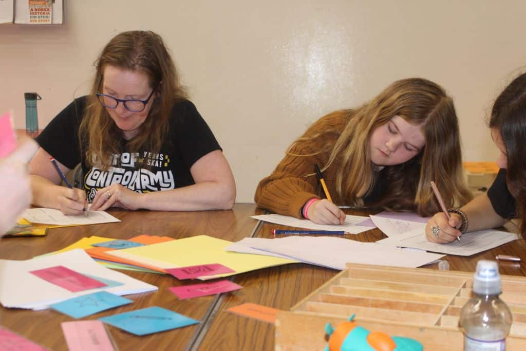 An adult and two older children taking part in a creative writing activity.