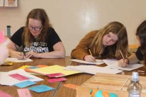 An adult and two older children taking part in a creative writing activity.