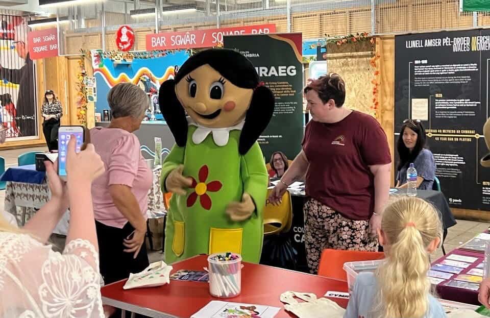 Mascot Magi Ann visiting our flexi-space area. People are gathered around to take photos.